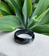 Black bracelet on a textured surface with green leaves in the background