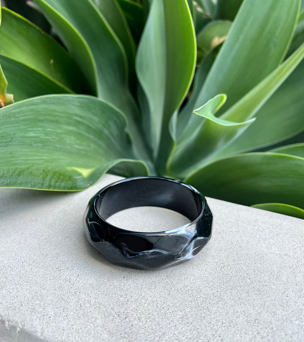 Black bracelet on a textured surface with green leaves in the background