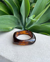 Tortoiseshell resin bracelet a white surface with green leaves in the background