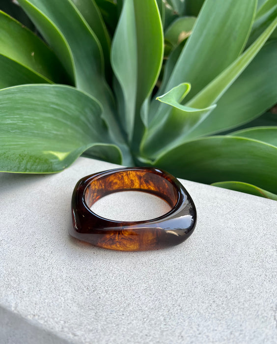 Tortoiseshell resin bracelet a white surface with green leaves in the background