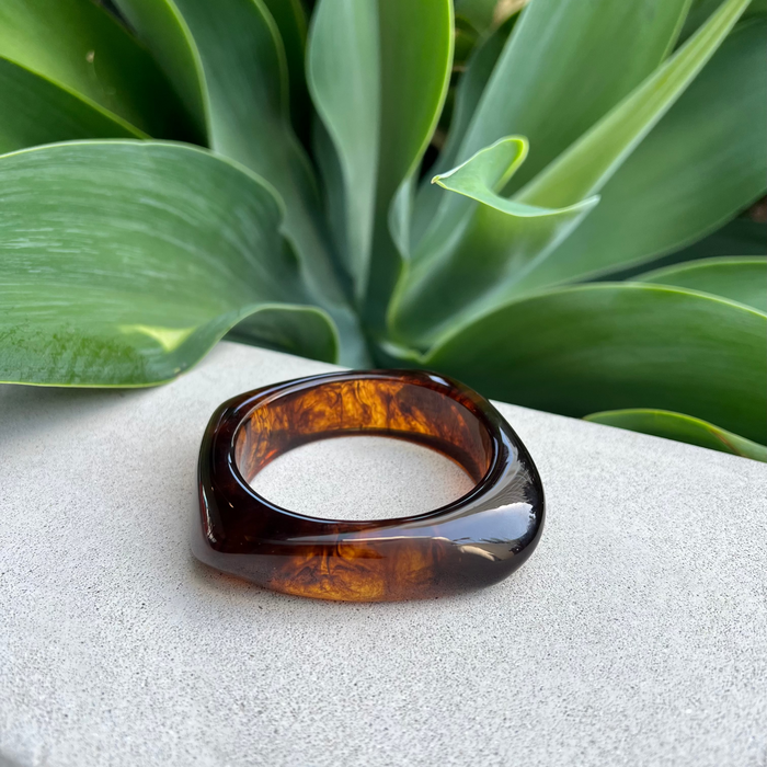 Tortoiseshell resin bracelet a white surface with green leaves in the background