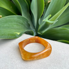 Brown bangle on a textured surface with green leaves in the background