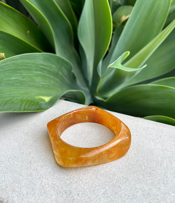 Brown bangle on a textured surface with green leaves in the background