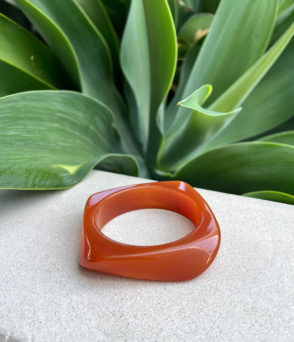 Orange bangle on a textured surface with green leaves in the background