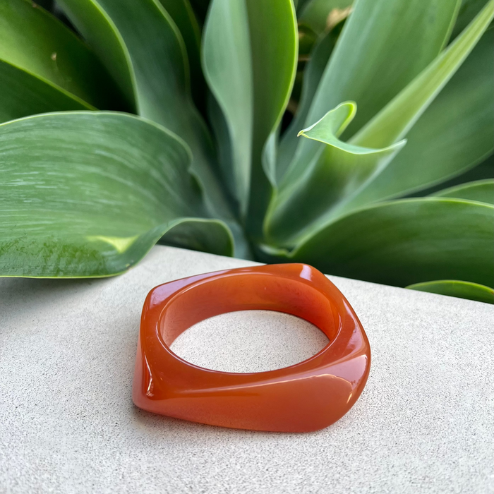 Orange bangle on a textured surface with green leaves in the background