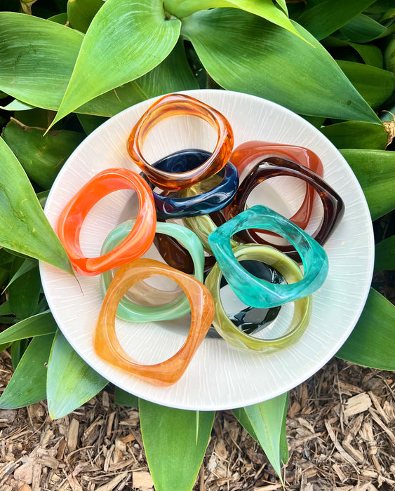 Colorful resin bracelets on a white plate with green leaves in the background