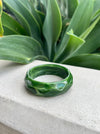 Green bracelet on a stone surface with a plant in the background