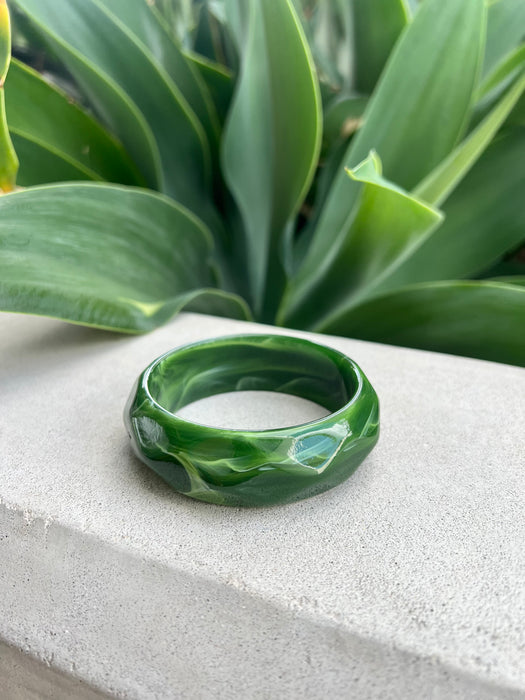 Green bracelet on a stone surface with a plant in the background