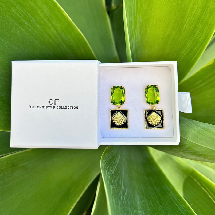 Green gemstone earrings in a white box with 'The Christy F Collection' branding, placed on green leaves.