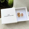 A gold-trimmed open ring with rectangular and round pink gemstones, presented in a white box from The Christy F Collection.