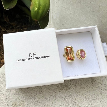 A gold-trimmed open ring with rectangular and round pink gemstones, presented in a white box from The Christy F Collection.