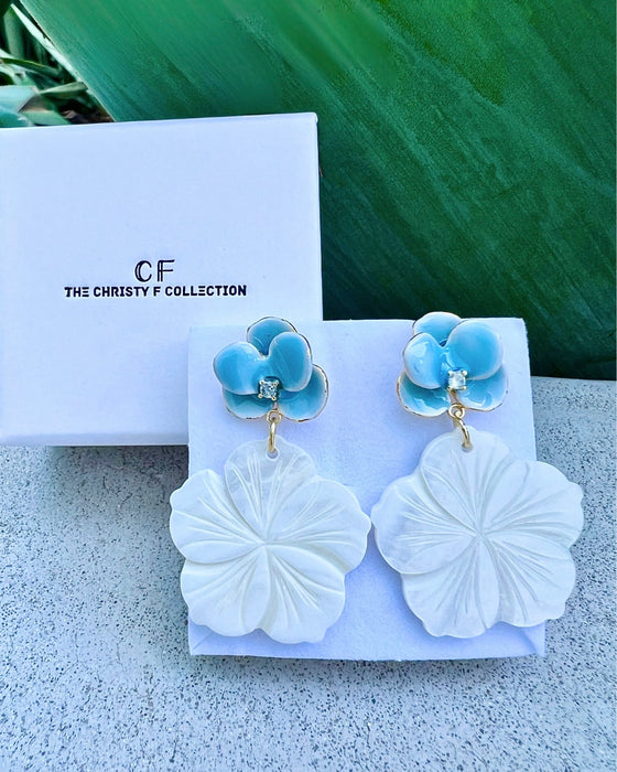 Pair of earrings with blue floral tops and white leaf-like bottoms on a branded display card.
