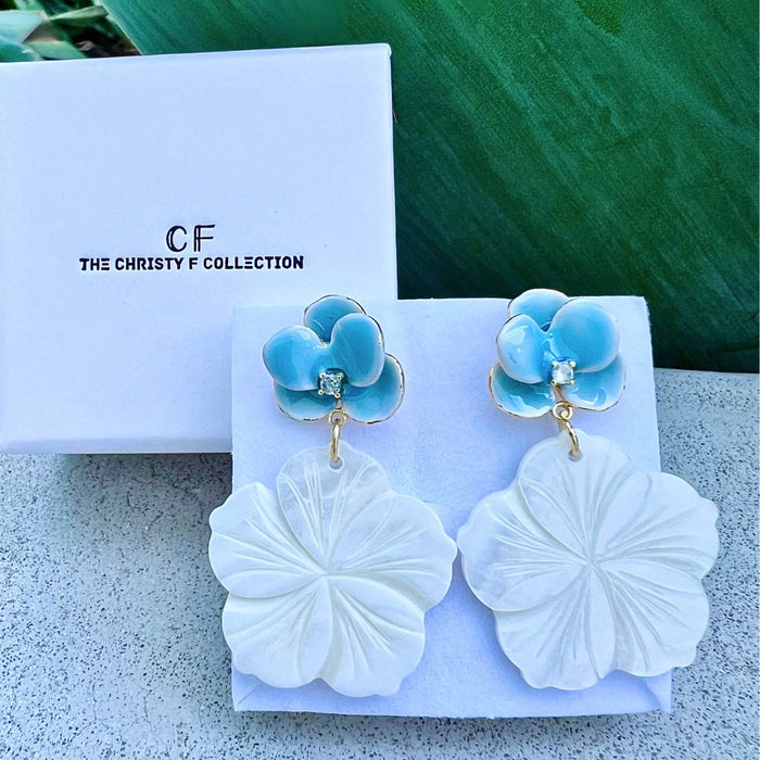 Pair of earrings with blue floral tops and white leaf-like bottoms on a branded display card.