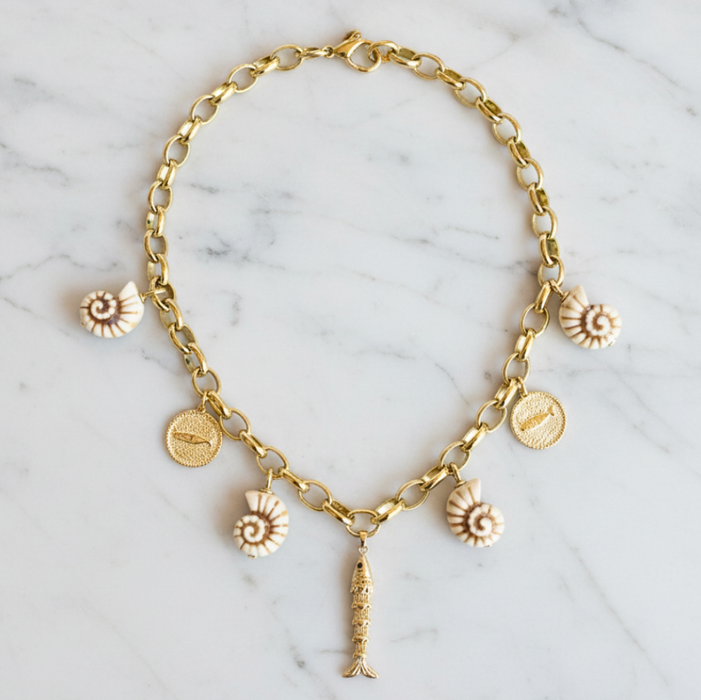 Gold chain necklace with various charms on a marble surface
