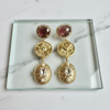 Gold earrings with gemstones on a clear glass tray against a marble background