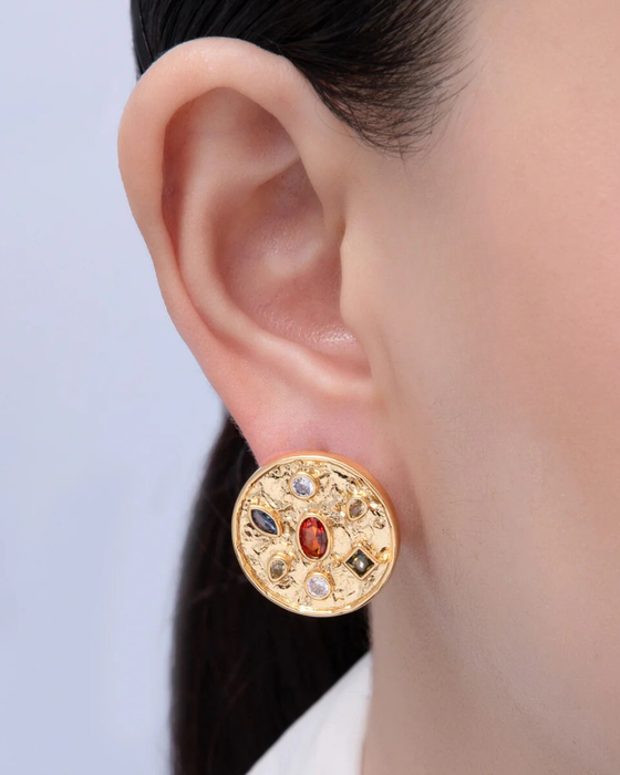 Gold earring with gemstones worn by a person against a light background