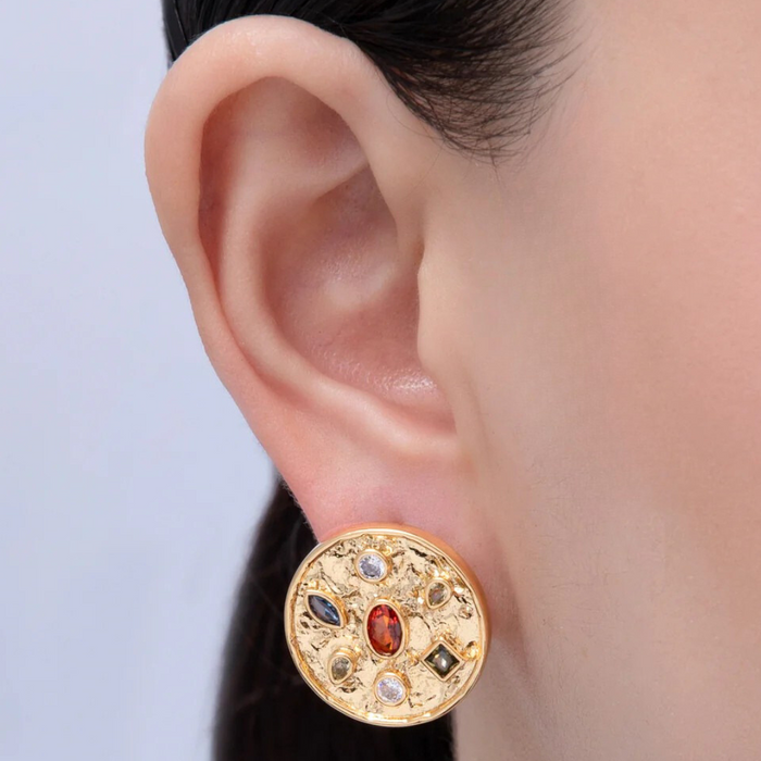 Gold earring with gemstones worn by a person against a light background