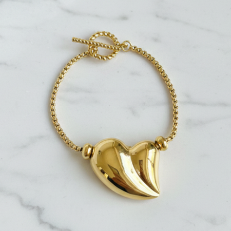 Gold bracelet with a heart-shaped pendant on a marble surface