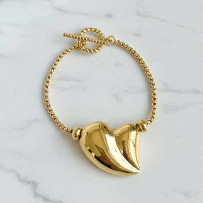 Gold bracelet with a heart-shaped pendant on a marble surface