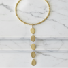 A gold-toned twisted rope collar necklace with a vertical drop of five textured oval and teardrop charms, displayed flat on a white marble surface.