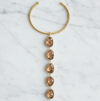 A gold-toned twisted cable cuff necklace with a vertical dangle featuring five faceted smoky amber gemstones, displayed flat on a white marble background.