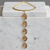 A gold-toned necklace with a circular cuff-style top and five dangling faceted amber gemstones, displayed on a white marble block against a gray background.