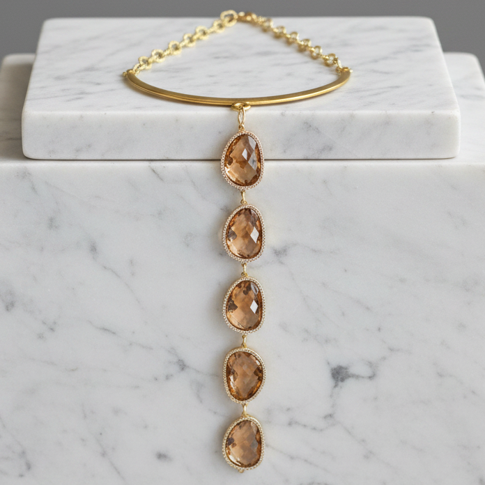 A gold-toned necklace with a circular cuff-style top and five dangling faceted amber gemstones, displayed on a white marble block against a gray background.