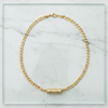 Gold chain necklace with a cylindrical pendant on a marble surface
