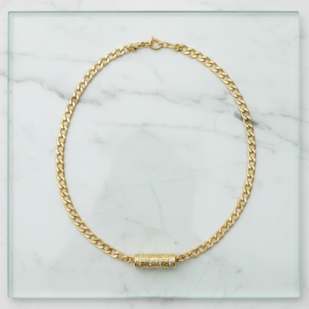 Gold chain necklace with a cylindrical pendant on a marble surface