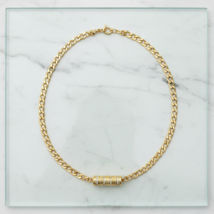 Gold chain necklace with a cylindrical pendant on a marble surface
