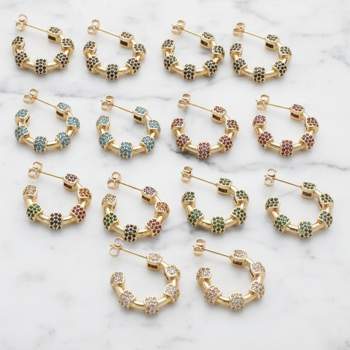Set of gold hoop earrings with colorful gemstones on a marble surface
