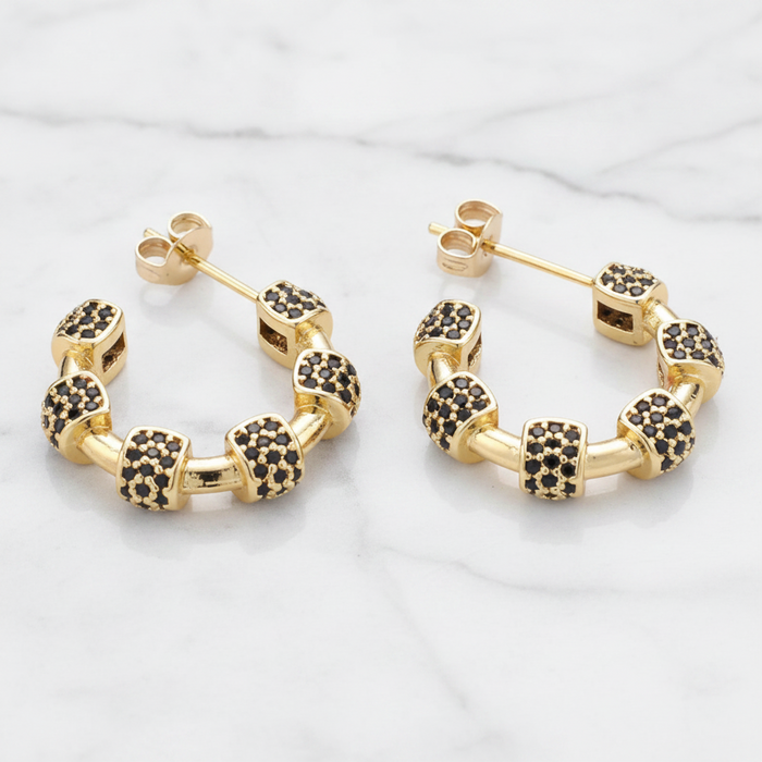 Gold hoop earrings with black gemstones on a light gray background