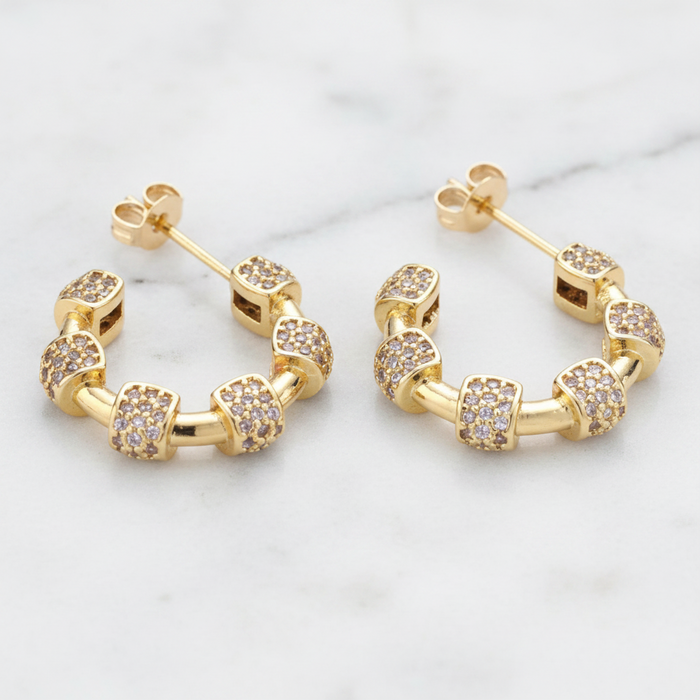 Gold hoop earrings with embedded stones on a light background