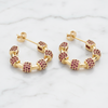 Gold hoop earrings with red gemstones on a marble surface