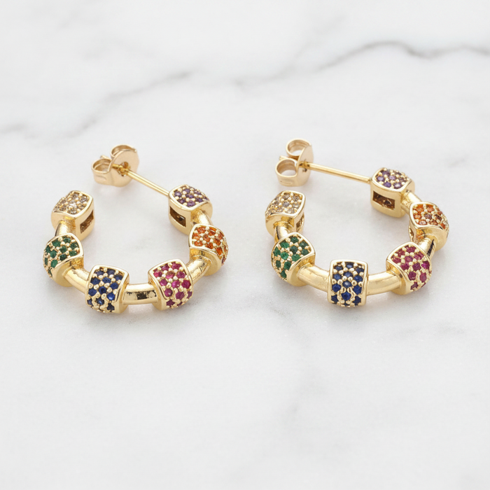 Gold hoop earrings with multicolored gemstones on a light background