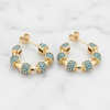 Gold hoop earrings with blue gemstones on a marble background