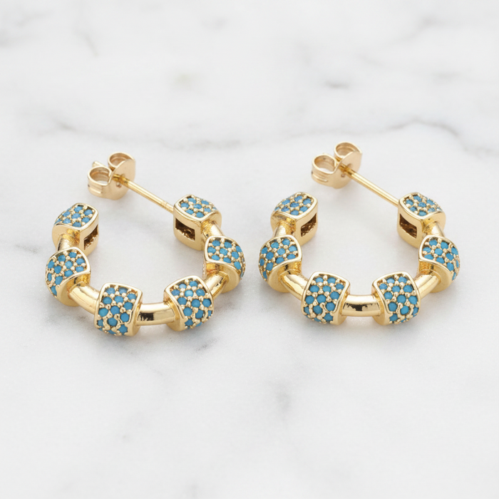 Gold hoop earrings with blue gemstones on a marble background