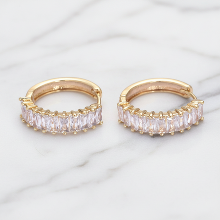Gold hoop earrings with clear gemstones on a marble surface