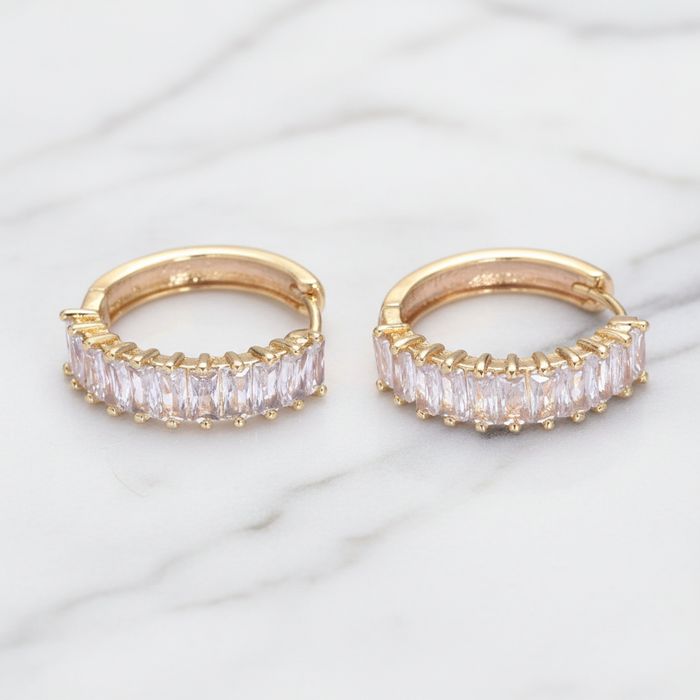 Gold hoop earrings with clear gemstones on a marble surface