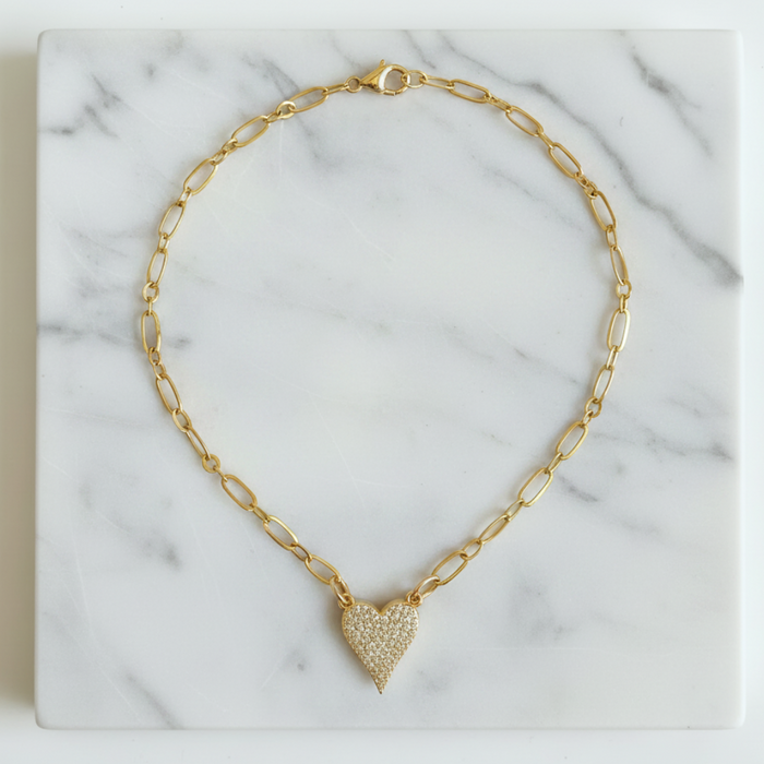 Gold chain necklace with a heart-shaped pendant on a marble surface