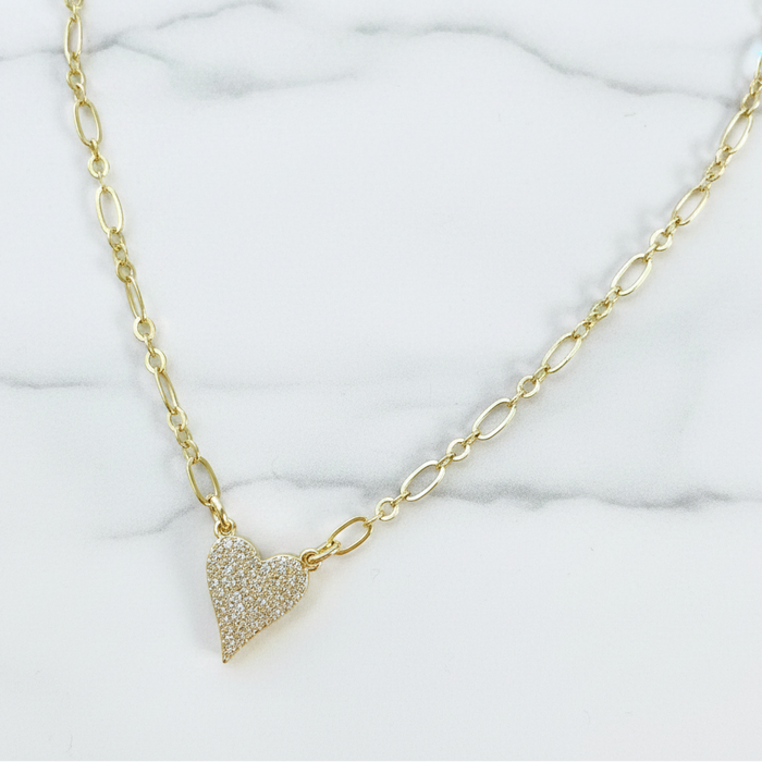 Gold necklace with a heart-shaped pendant on a marble background