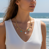 Woman wearing a gold necklace with charms against a beach background