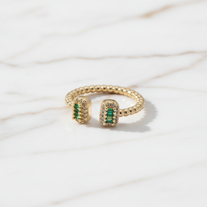 Gold ring with green gemstones on a light background