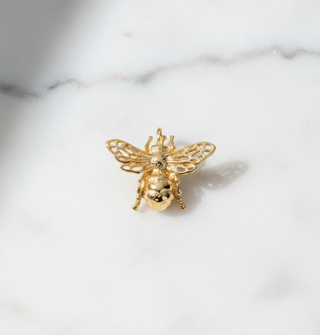 Gold bee-shaped brooch on a marble surface