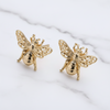 Gold bee-shaped earrings on a marble surface
