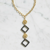 Gold and black geometric necklace on a marble surface