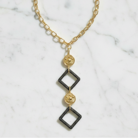 Gold and black geometric necklace on a marble surface