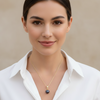 Woman wearing a white shirt and gold necklace with a dark pendant against a beige background