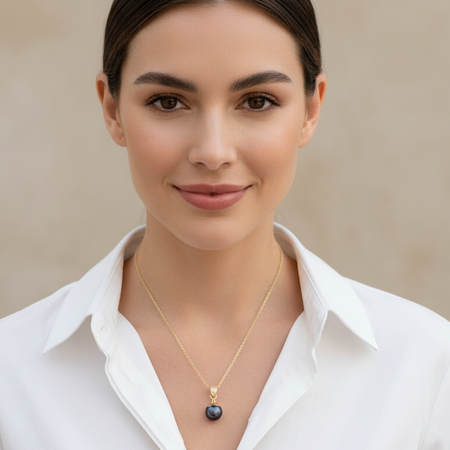 Woman wearing a white shirt and gold necklace with a dark pendant against a beige background