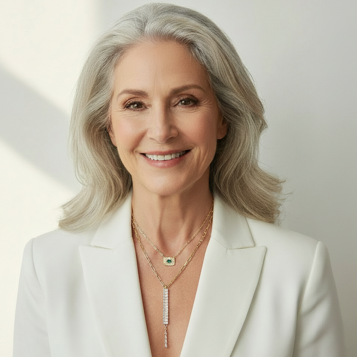 Woman wearing a white blazer and gold jewelry against a light background